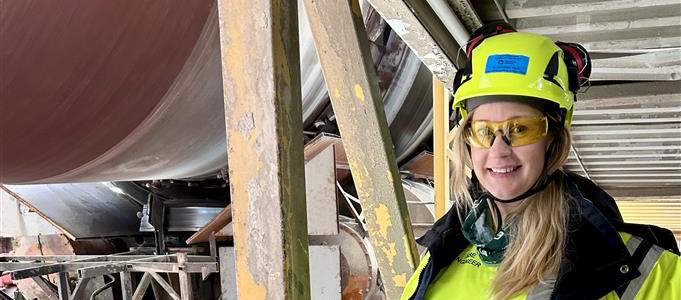 Anställd i skyddsutrustning bredvid industriell utrustning på cementfabrik.