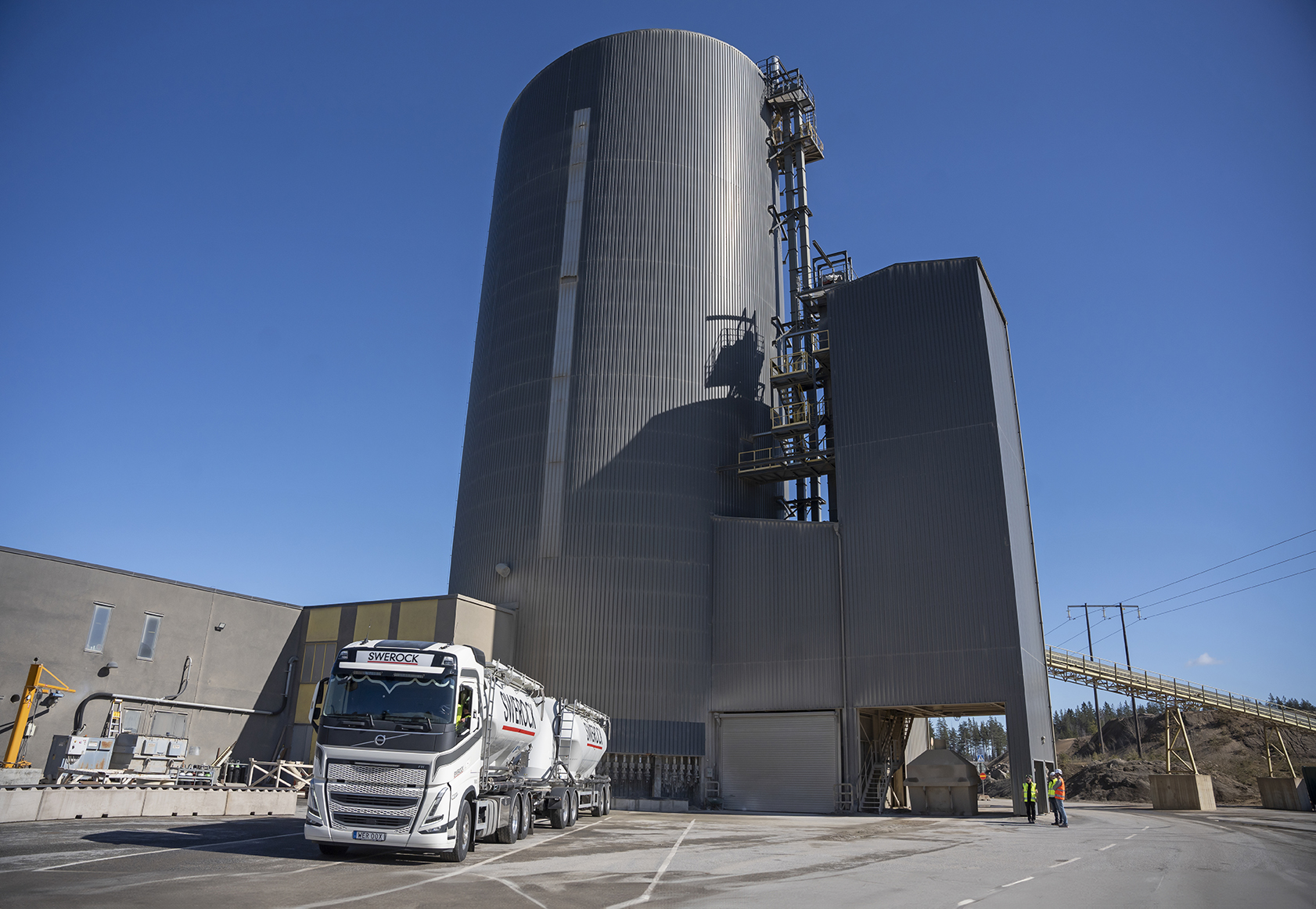 En industribyggnad med höga silotorn och en lastbil parkerad framför.