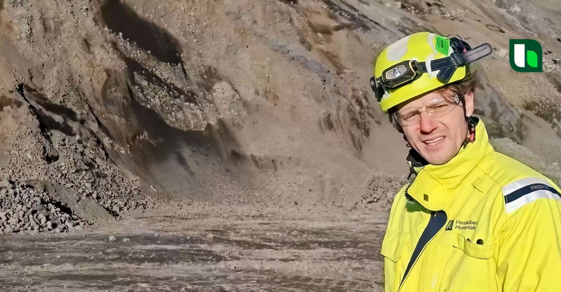 Worker in high-visibility clothing and helmet standing near a rocky quarry site.