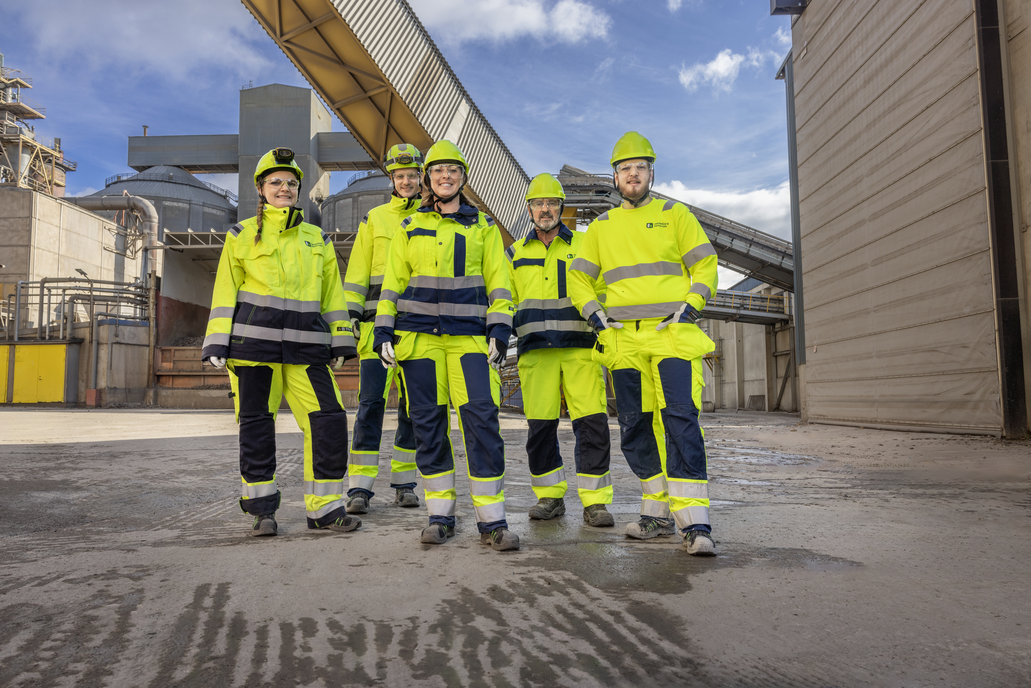 En grupp arbetsklädda arbetare står framför en industriell byggnad.
