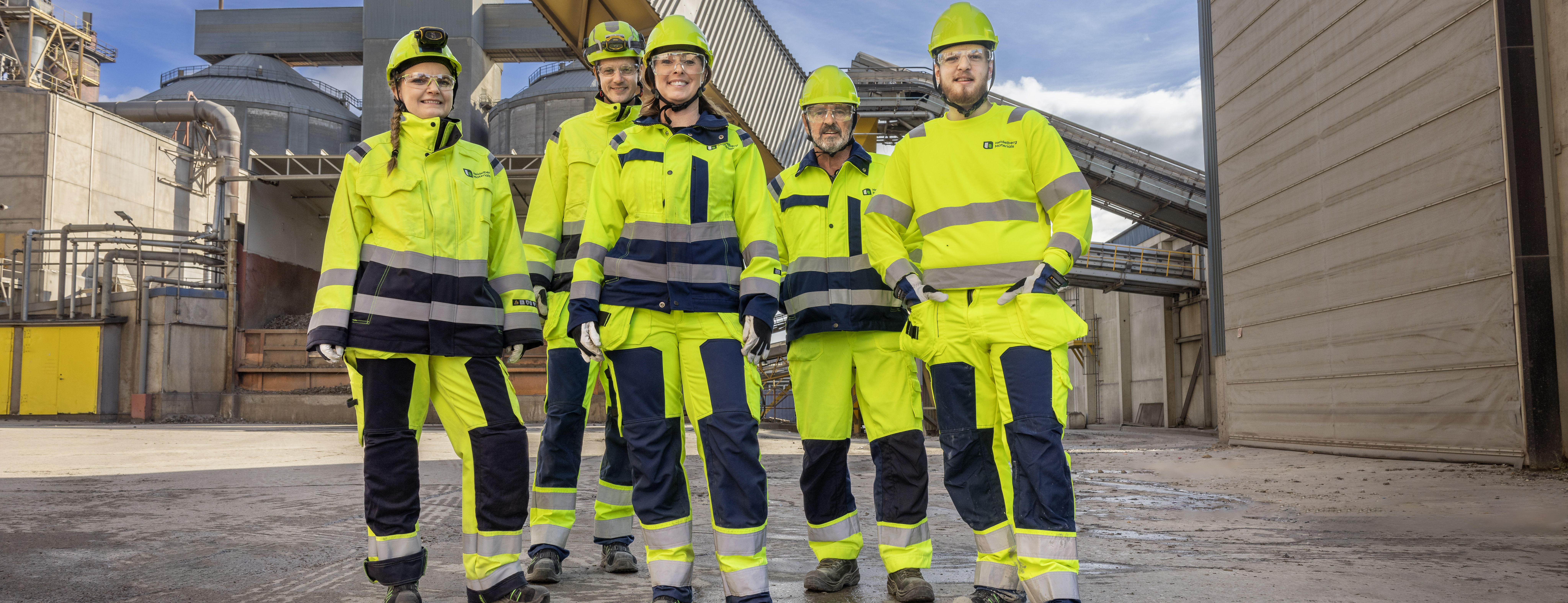 En grupp arbetsklädda arbetare står framför en industriell byggnad.