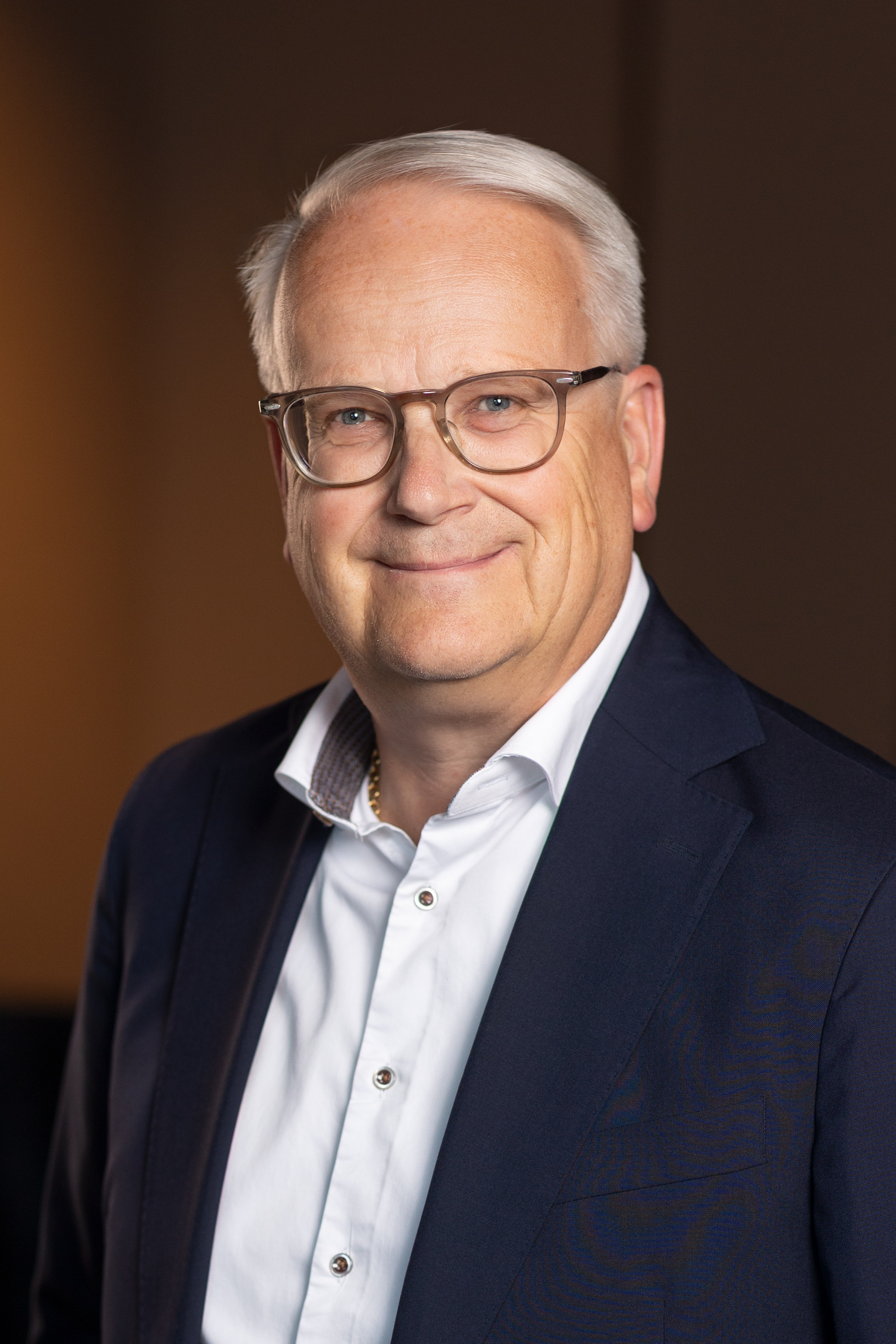 En affärsklädd man med glasögon står inomhus och ser mot kameran.