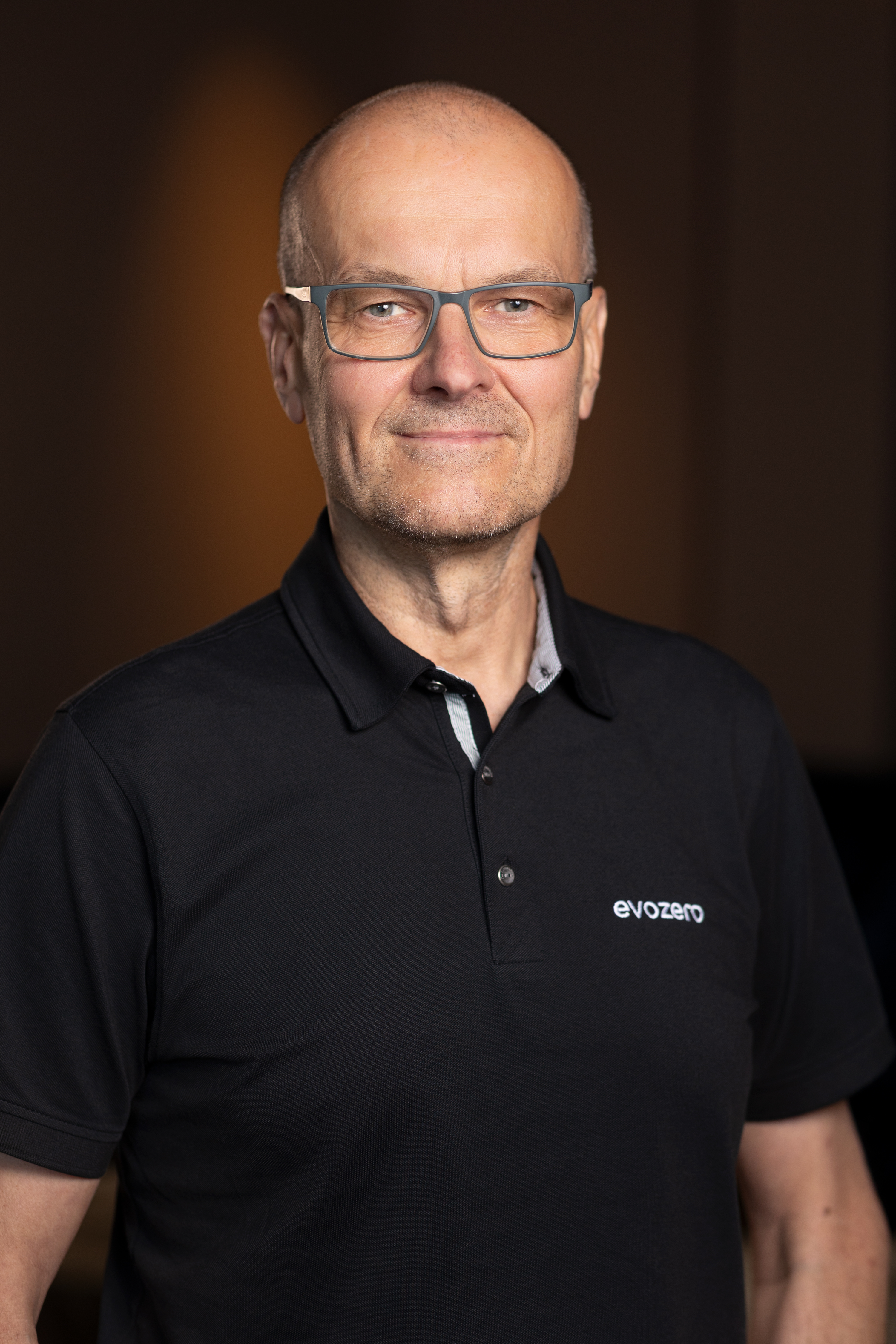 En man i svart pikétröja med företagslogotyp, fotograferad inomhus.