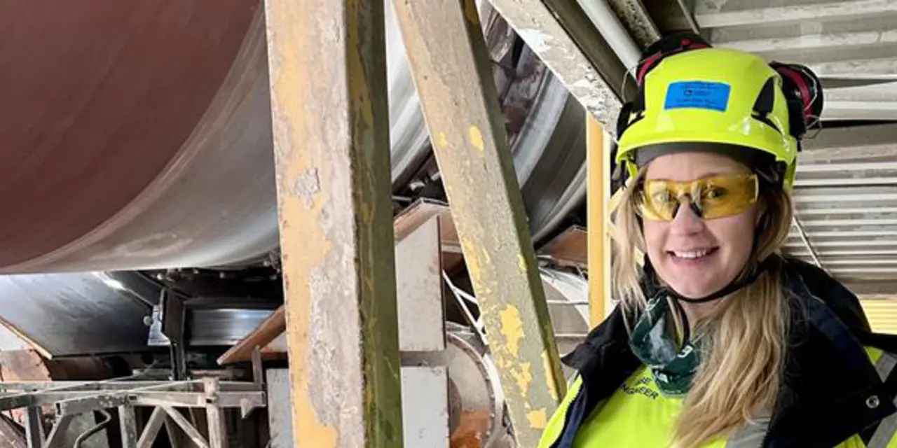 Anställd i skyddsutrustning bredvid industriell utrustning på cementfabrik.