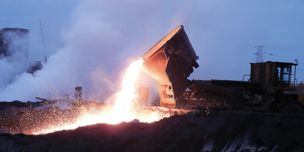 Maskin tömmer glödande material på en industriell plats i skymningsljus.