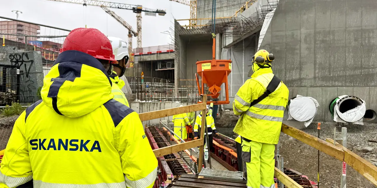 Byggarbetsplats med arbetare i gula skyddskläder och hjälmar nära betongkonstruktioner.