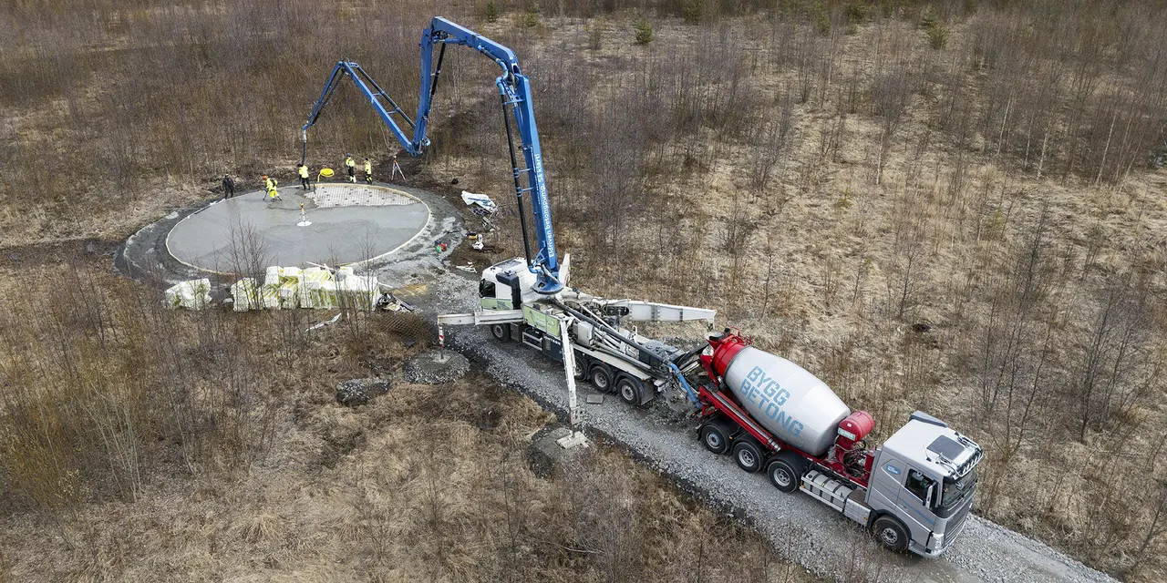 Betongpump och betonglastbil vid byggarbetsplats omgiven av skog.