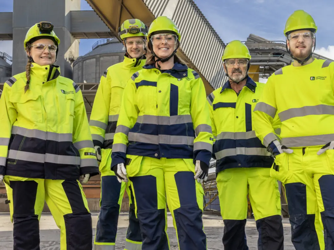 En grupp arbetsklädda arbetare står framför en industriell byggnad.