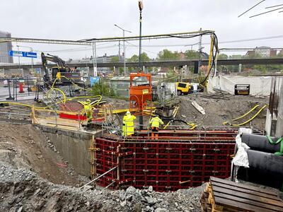 Byggarbetsplats med två arbetare i säkerhetskläder som står vid en form för betonggjutning.