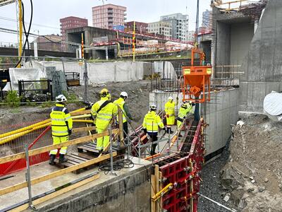Byggarbetare i skyddsutrustning arbetar vid en byggarbetsplats med betongkonstruktioner.