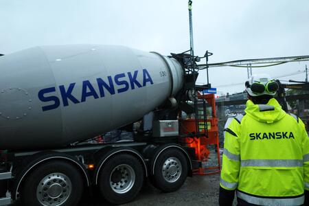 En betonglastbil och en arbetare med Skanska-logotyp på en byggarbetsplats.